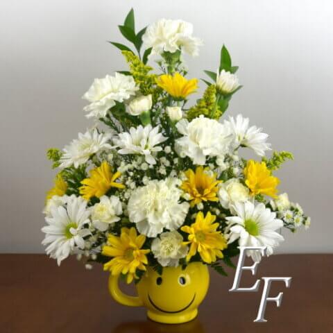 Floral arrangement in a yellow happy face mug