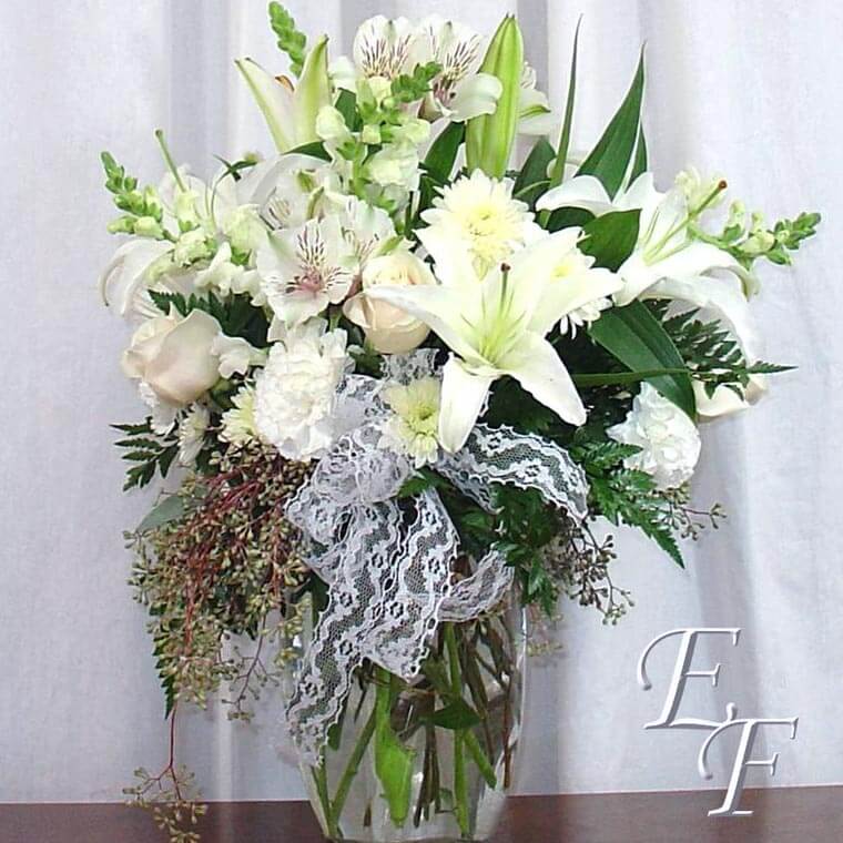 White Oriental Lilies, Alstromeria, Roses, Snapdragons, and Carnations are arranged in a 9″ Vase.